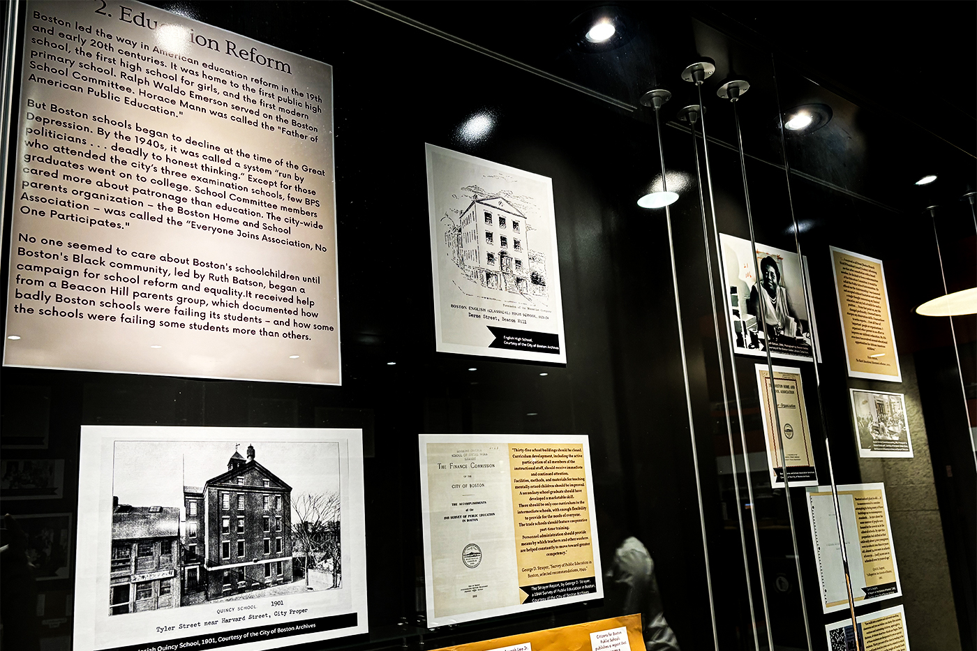 Archival documents and photos displayed in a glass gallery wall. 