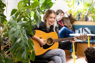 A person plays guitar while surrounded by greenery.