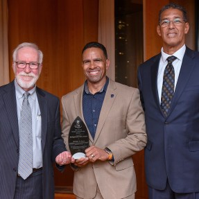 Mike Davis holding his award posing with two other people.