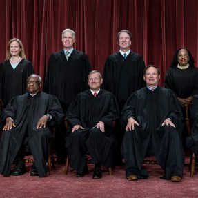 Group photo of the U.S. Supreme Court justices sitting and standing before a red curtain.