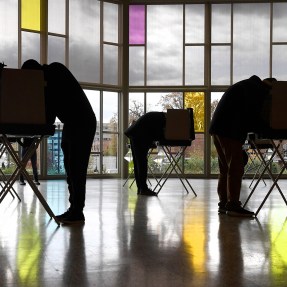 Silhouette of several voters bent over tables as they vote in Connecticut.