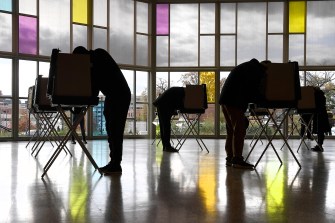 Silhouette of several voters bent over tables as they vote in Connecticut.