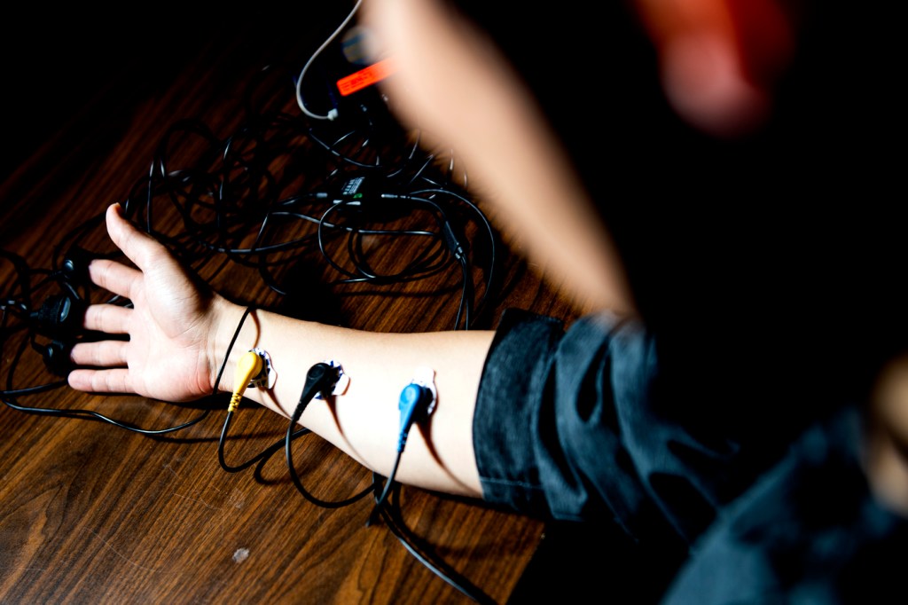 A person holding out their arm with their sleeve rolled up, several wires attached to their forearm to measure pain.