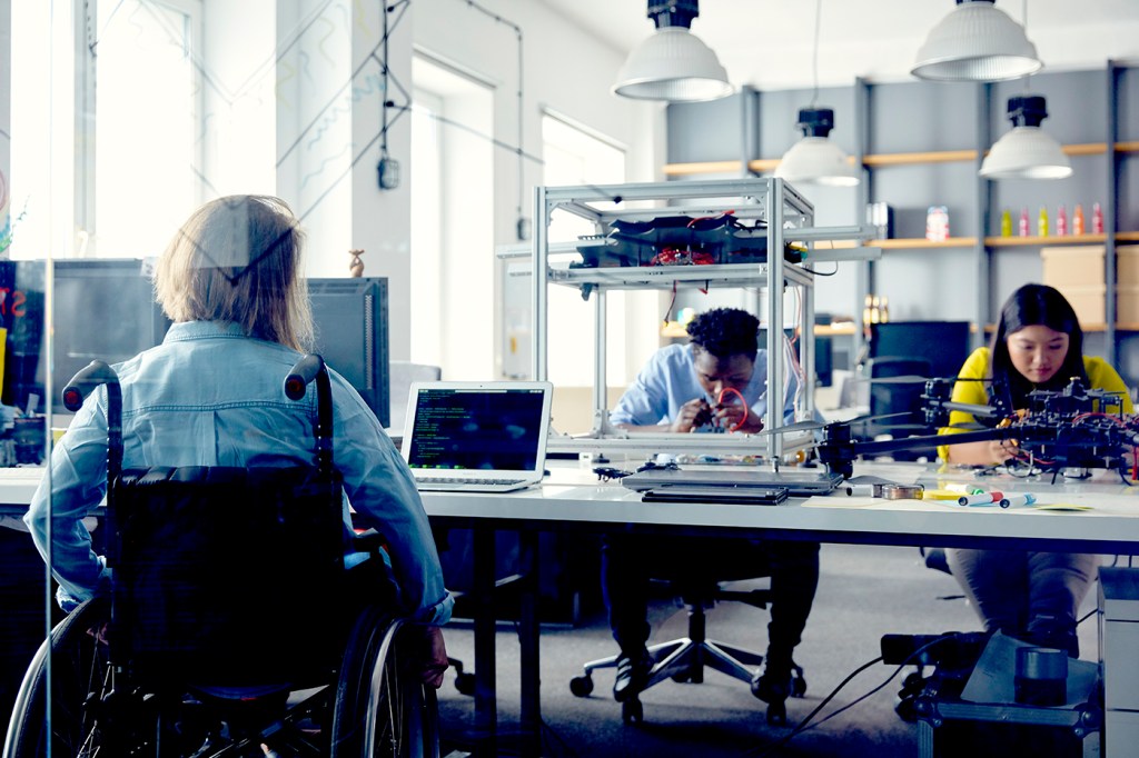 A person on a wheelchair working at a lab table with two other people.