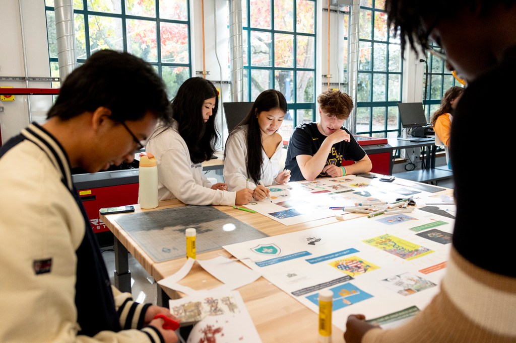 Students collaborating on a creative project at a large work table in a well-lit workshop space.