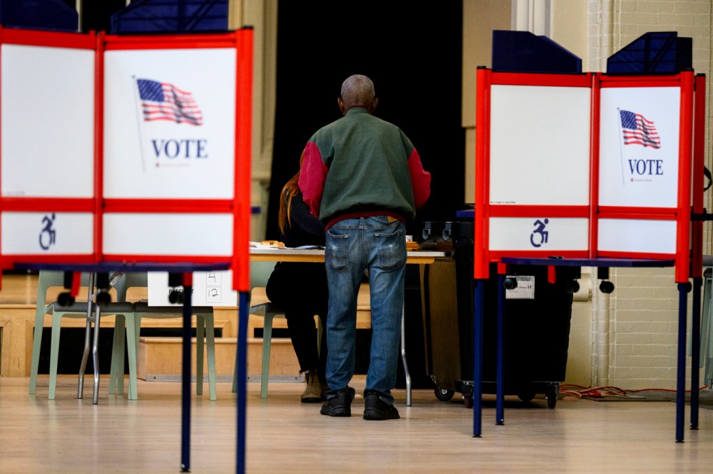 A person votes at a booth in Northeastern's Fenway Center, with visible American flag 'VOTE' signs.