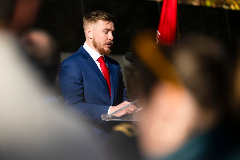 A person wearing a blue suit and red tie speaking at a podium.