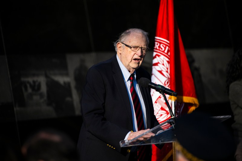 A speaker at a podium in front of a Northeastern flag.
