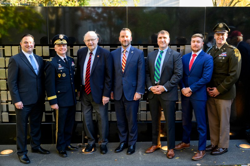 A group of people poses for a photo in front of the Veterans memorial.