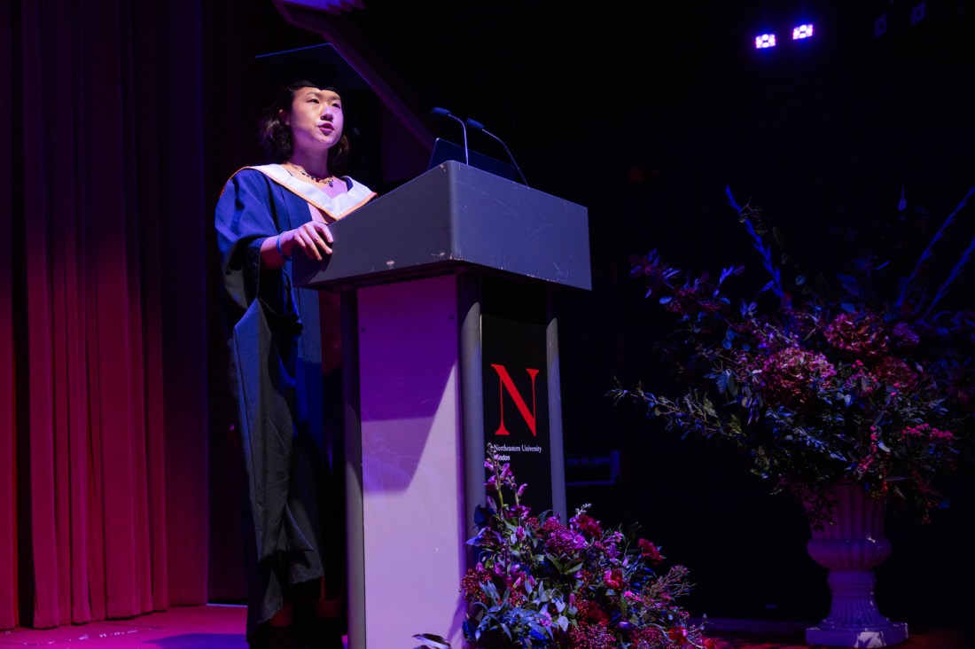 Xiaoya Huang speaking at a podium in the Barbican Centre.