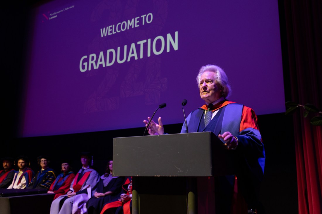 Anthony C. Grayling speaking at a podium in front of a screen that says 'Welcome to Graduation' on it in all caps. 