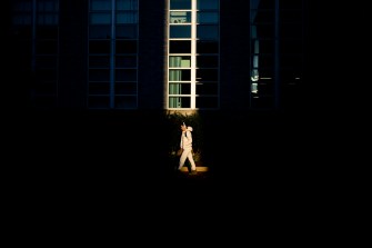 A person walking in front of a building with sunlight highlighting their path.