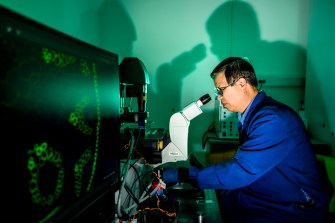 A researcher looks through a microscope inside a lab.