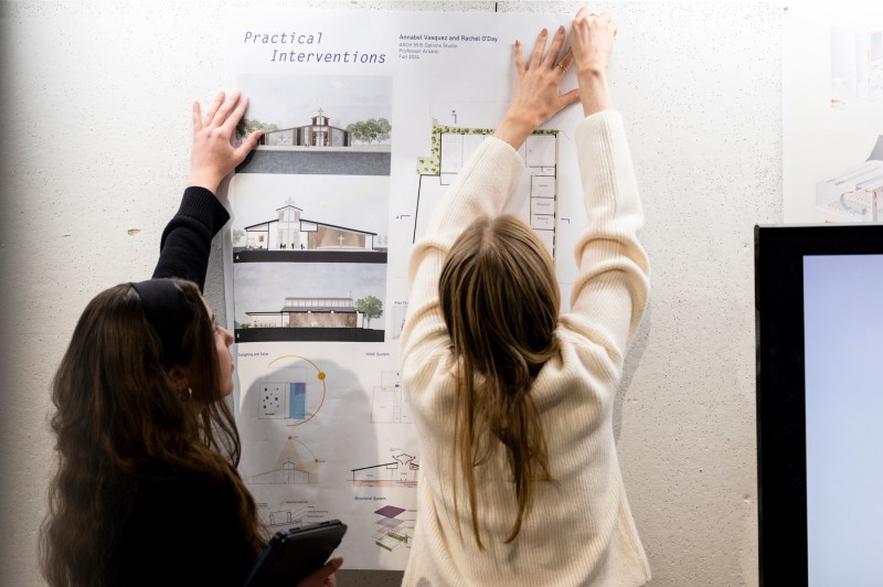 Students hanging architectural designs on a wall.