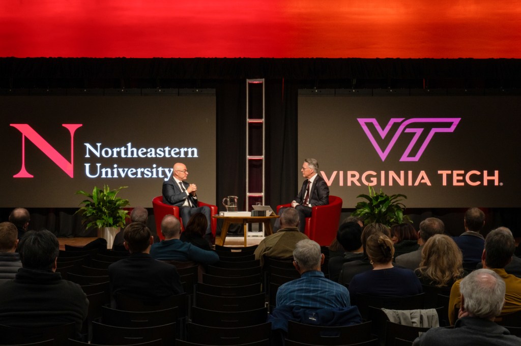 Two people engaged in a conversation on stage during an event, with an audience seated in front of them.