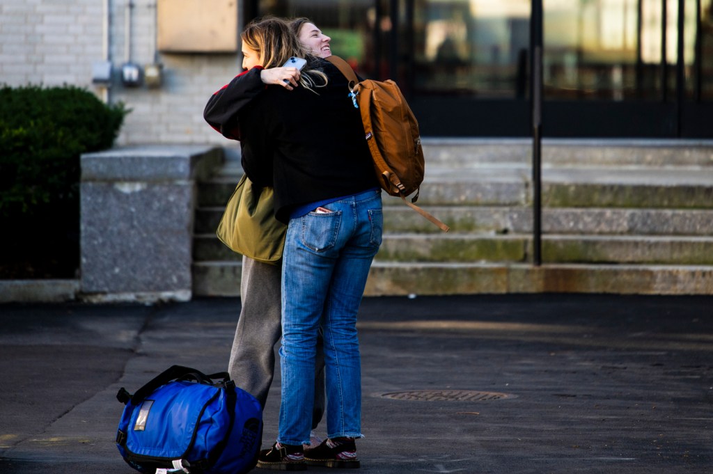 Two people embrace outdoors near a building, with luggage on the ground beside them.