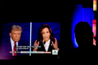 A person watches a TV screen airing a debate between former President Donald Trump (left) and Vice President Kamala Harris (right).