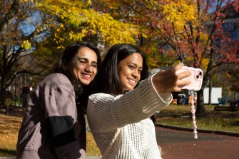 Two people standing outside taking a selfie on their phone.