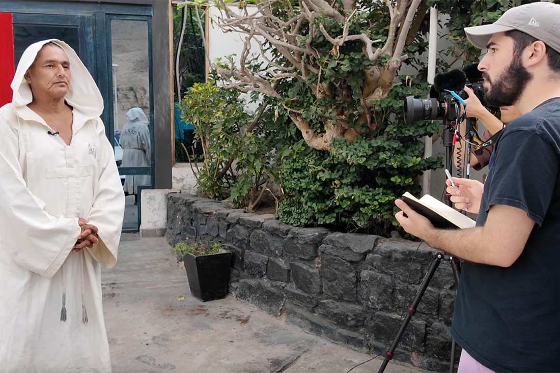 A student filming on a camera and another student writing in a notebook while talking to a Peruvian Cliff Diver.