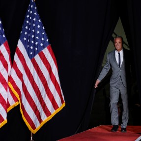 RFK standing on stage next to American flags.