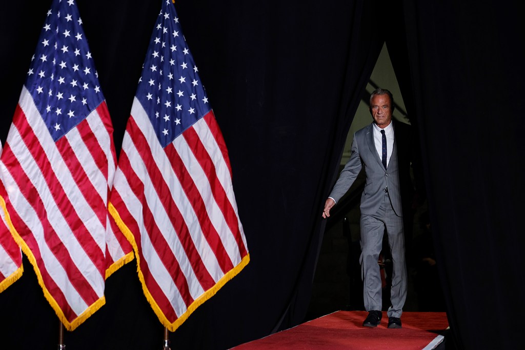 RFK standing on stage next to American flags.