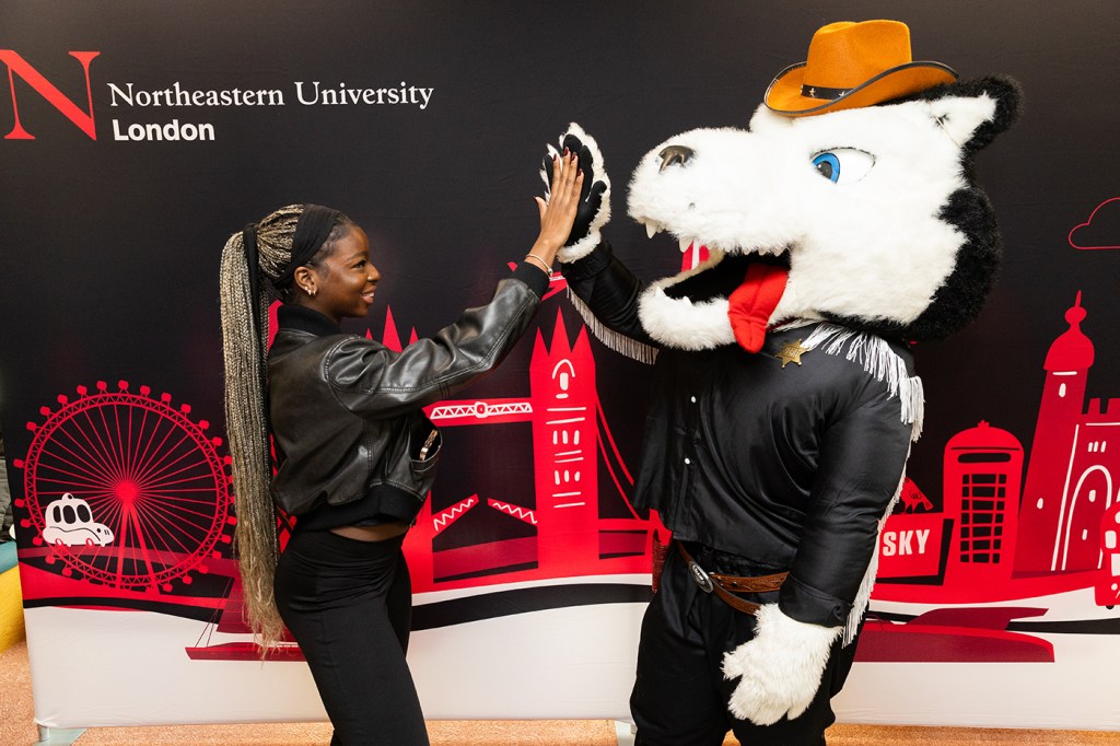 A person and a costumed mascot share a high five in front of a vibrant backdrop featuring iconic landmarks.