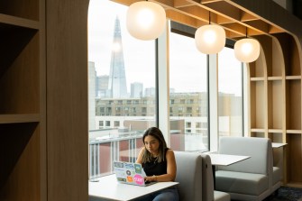 Student sits at a table by large windows with a view of London cityscape.