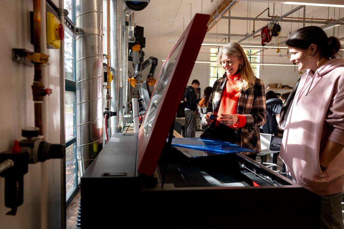 Two people interacting with equipment in a workshop or makerspace setting.