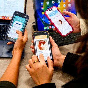 Three people's hands with their phones open to various pregnancy apps.