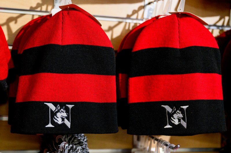 A closeup of black and red striped beanies with the Northeastern N and Husky.