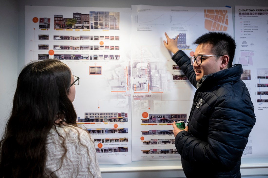 Wenchen Wang pointing to a poster displaying Stephanie Vojvodich's project and talking to her. In his other hand he is holding a canned drink. 