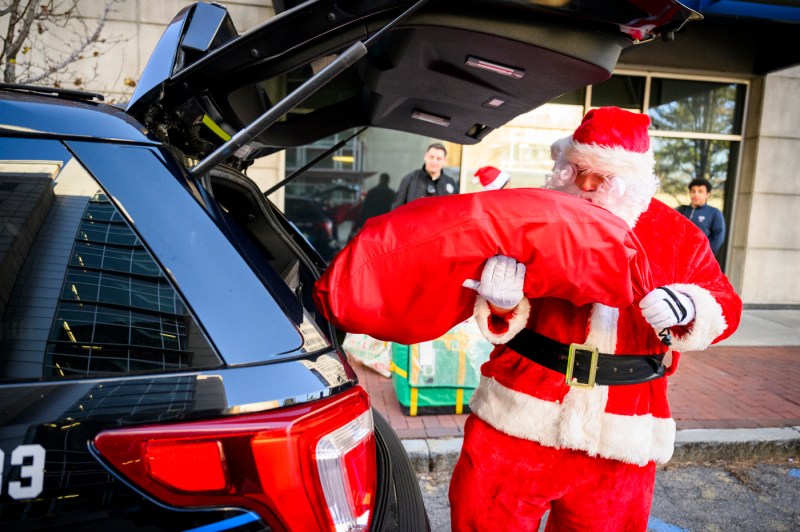 A person dressed as Santa Claus loading bags of toys into a car.