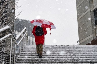 A person climbs the snowy stairs of the Interdisciplinary Science and Engineering Complex bridge as snow falls on Northeastern's Boston campus.