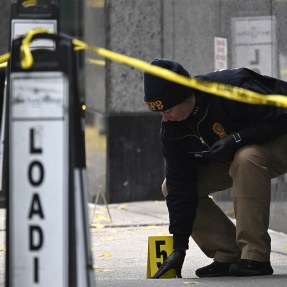 A police officer on the scene of a crime behind yellow caution tape.