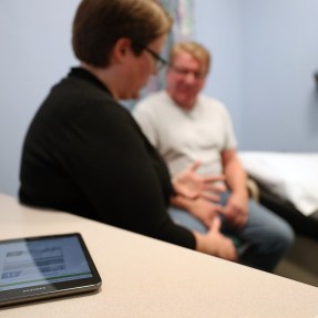 A health care professional talking with a patient. An iPad sits on a desk next to them.