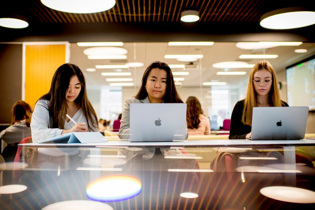 Three people sitting at a table next to each other working on laptops.