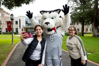 Students posing with a university mascot outdoors during an event.