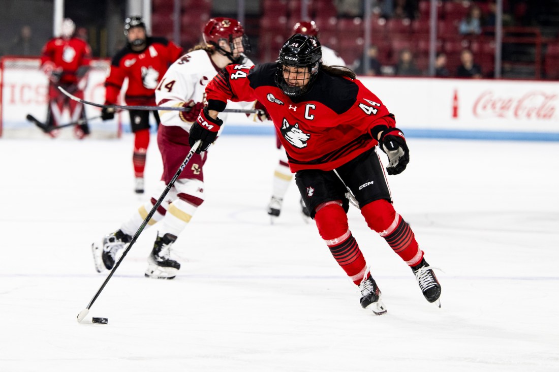 A Northeastern hockey player skating down the ice with the puck.