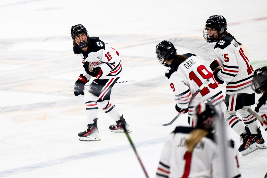 Northeastern womens hockey players smiling at each other while skating on the rink.