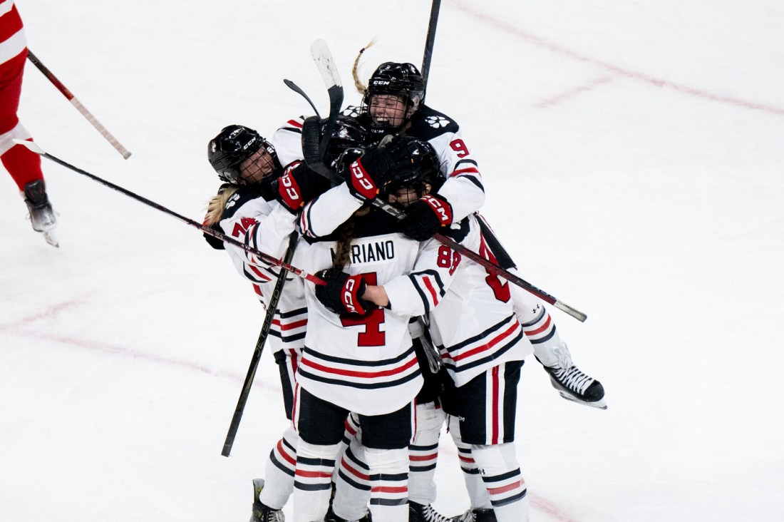 Northeastern womens hockey players jump on each other in celebration.