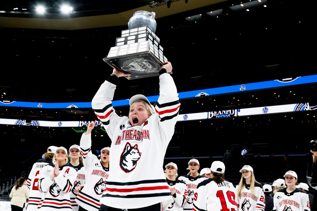 Women's hockey player holds the Beanpot trophy over their head