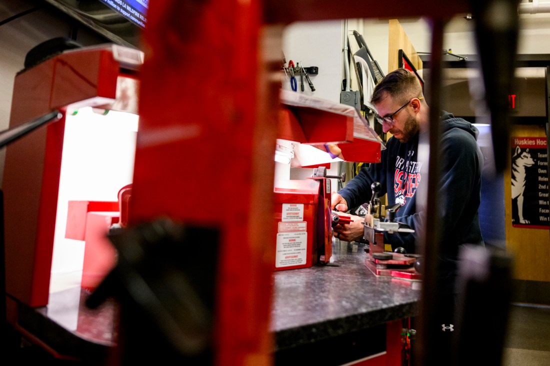 Dana Gobeil sharpening a hockey blade at a machine while wearing safety glasses.