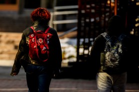 Two students seen from behind as they walk across campus wearing backpacks.
