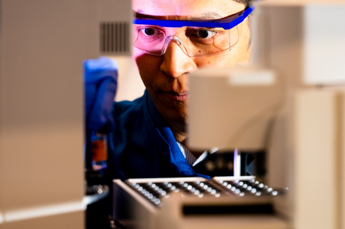 Jing-Ke Weng wearing safety glasses in a lab looking intently at a vial.