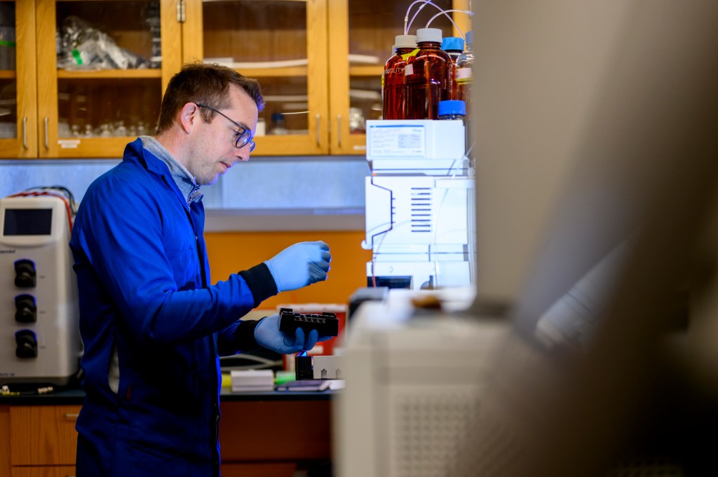 Benjamin Woolston sitting in his lab looking at a vial of substance.