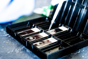 A black lab container with a series of slots and a pipette filling the slots with a test liquid.