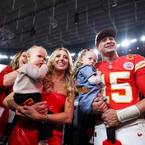 Patrick Mahomes wearing his Kansas City Chiefs Jersey, holding one of his kids. Next to him, his wife Brittany Mahones holds another one of their kids.