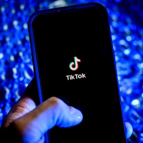 A person holding an iPhone with the TikTok app loading on screen.