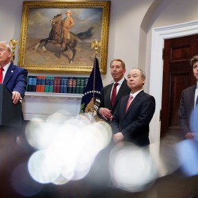 Donald Trump and several other men standing in a room at the white house. Donald Trump is standing behind a podium with a microphone.