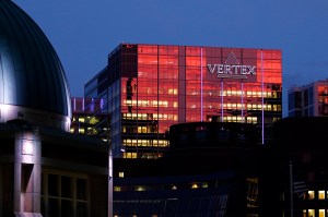 A glass building with 'Vertex' on the outside glows red in the sunset.